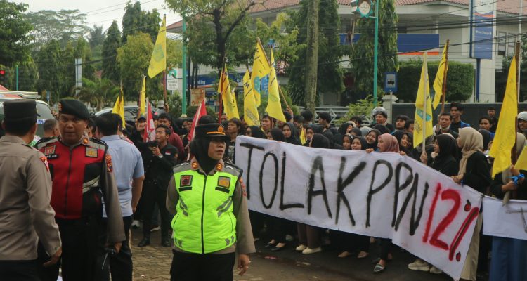 Demonstran melakukan aksi dengan membentangkan spanduk bertuliskan Tolak PPN 12%. (Aden/Fokuspers)